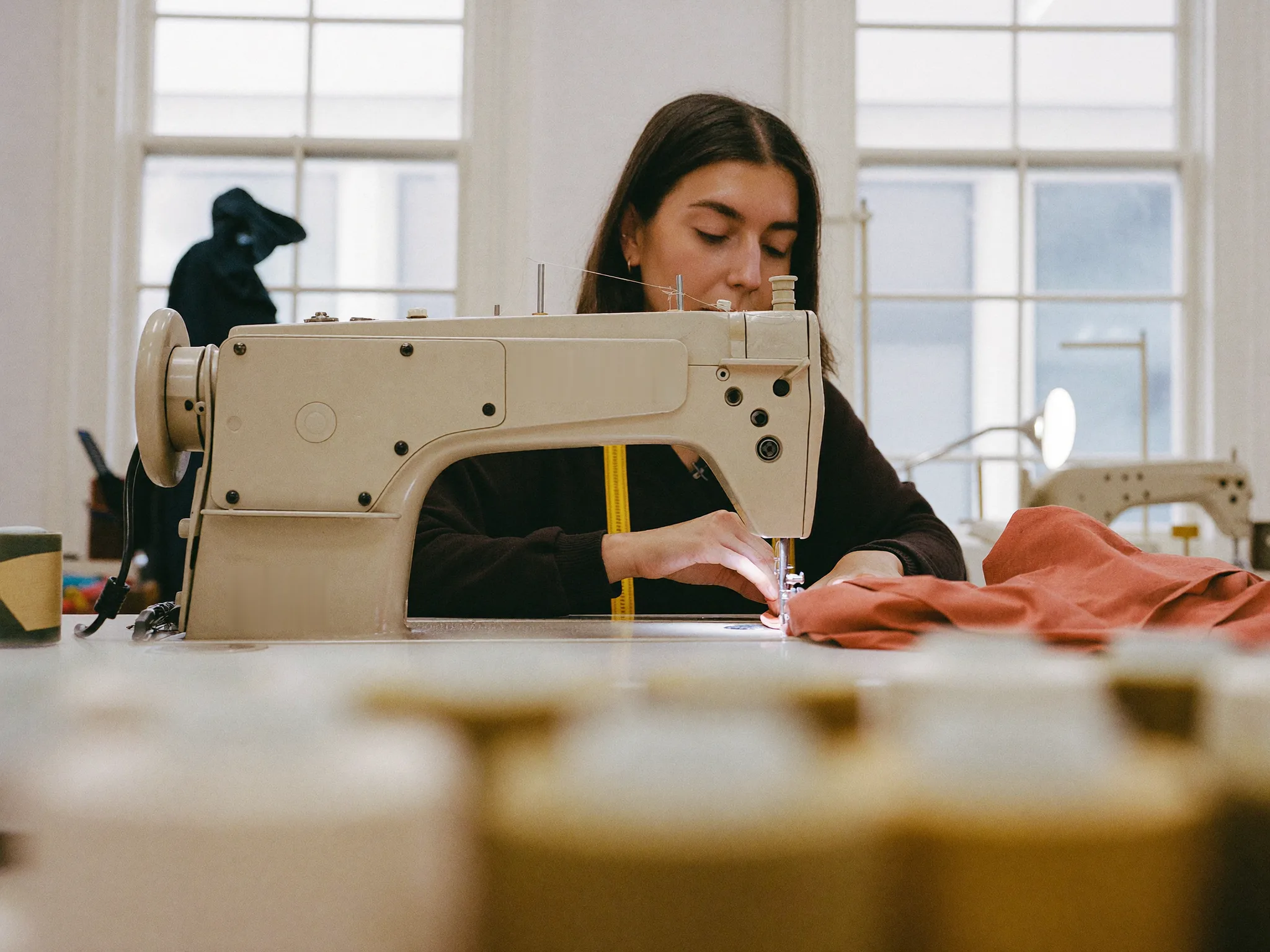 Seamstress sewing a first fit sample in terracotta stretch fabric in the sample room
